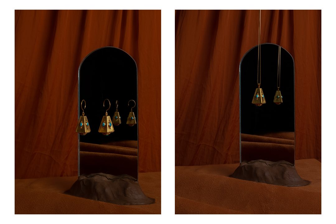 Gold earrings and a pendant hung before an arched mirror and a rust curtain