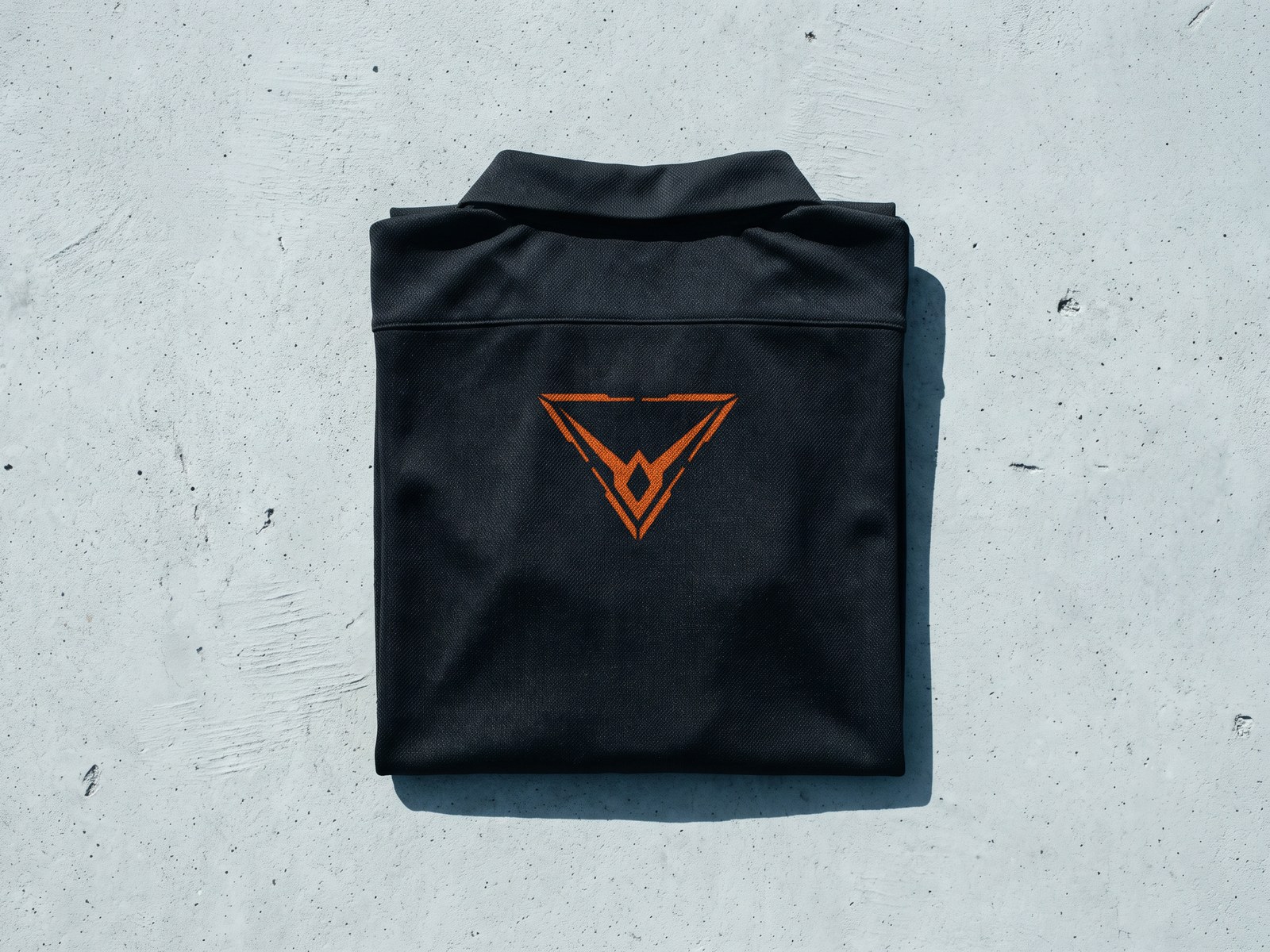 A render of a black training top folded square on concrete, the orange Hypereon mark on its chest