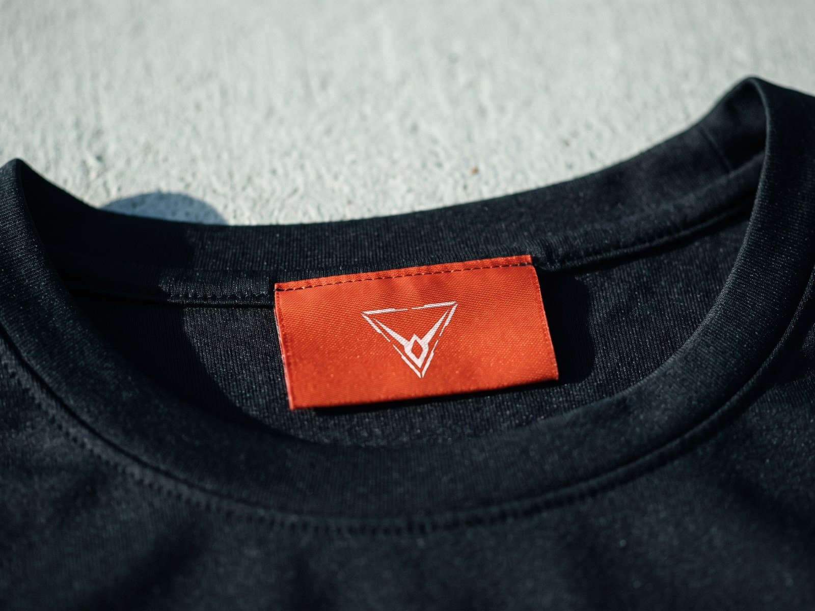 A render in close-up of an orange woven label inside the neck of a black top, the Hypereon mark in white