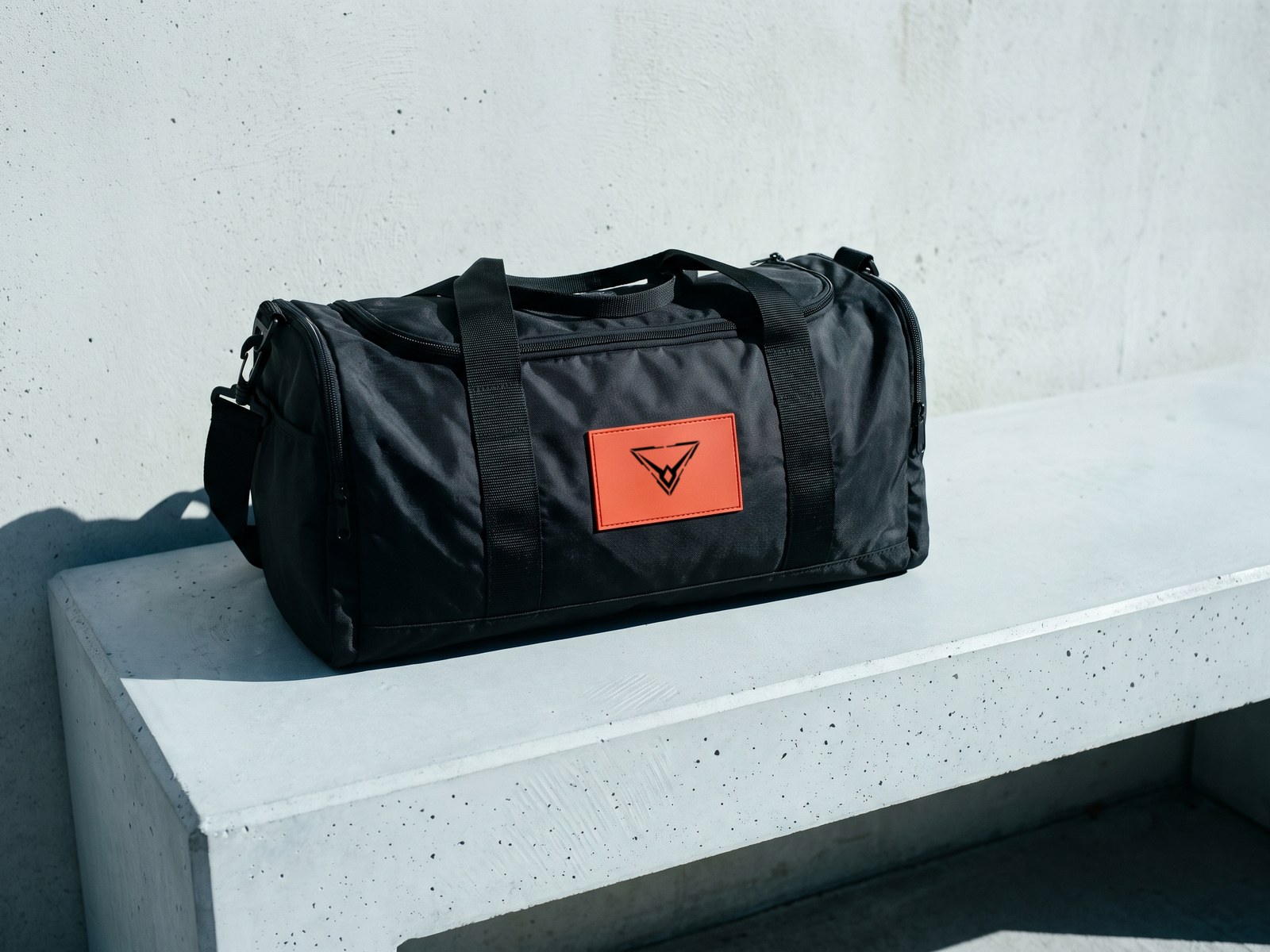 A render of a black duffel bag on a concrete bench, an orange patch on its side carrying the Hypereon mark in black