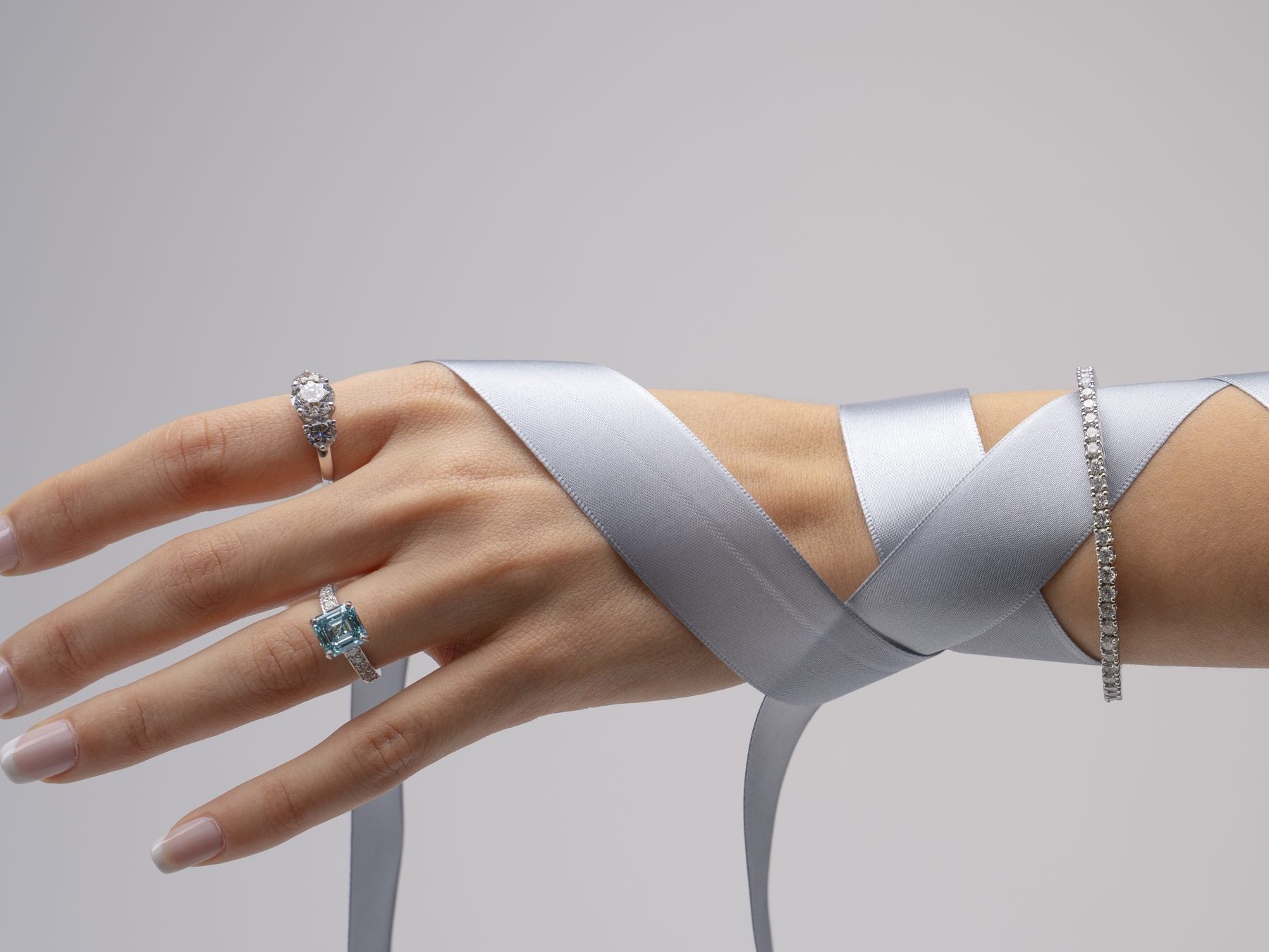 A grey satin ribbon wound round a hand wearing two rings and a bracelet