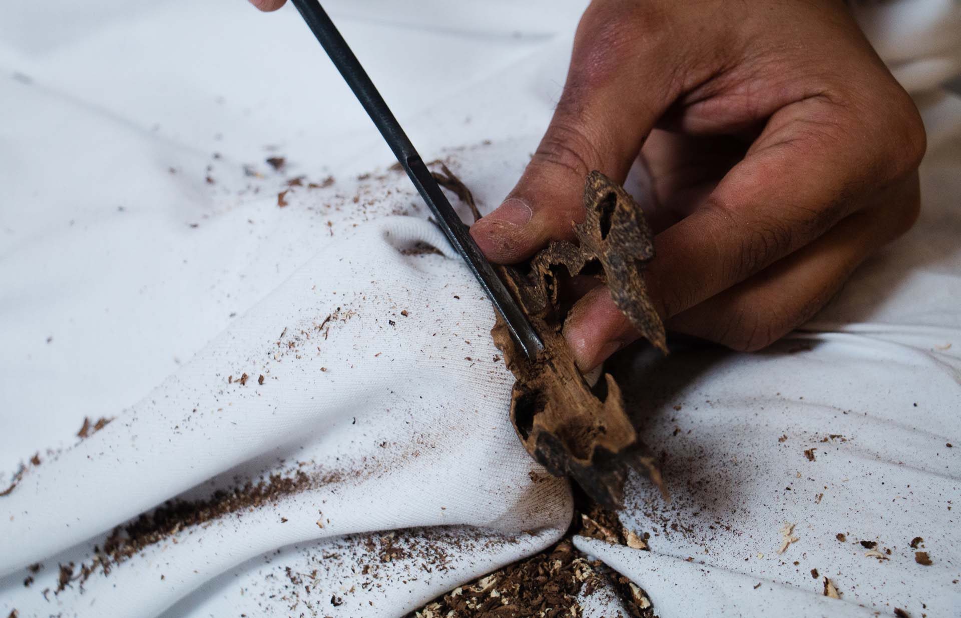 A metal pick cutting into a piece of agarwood on white cloth