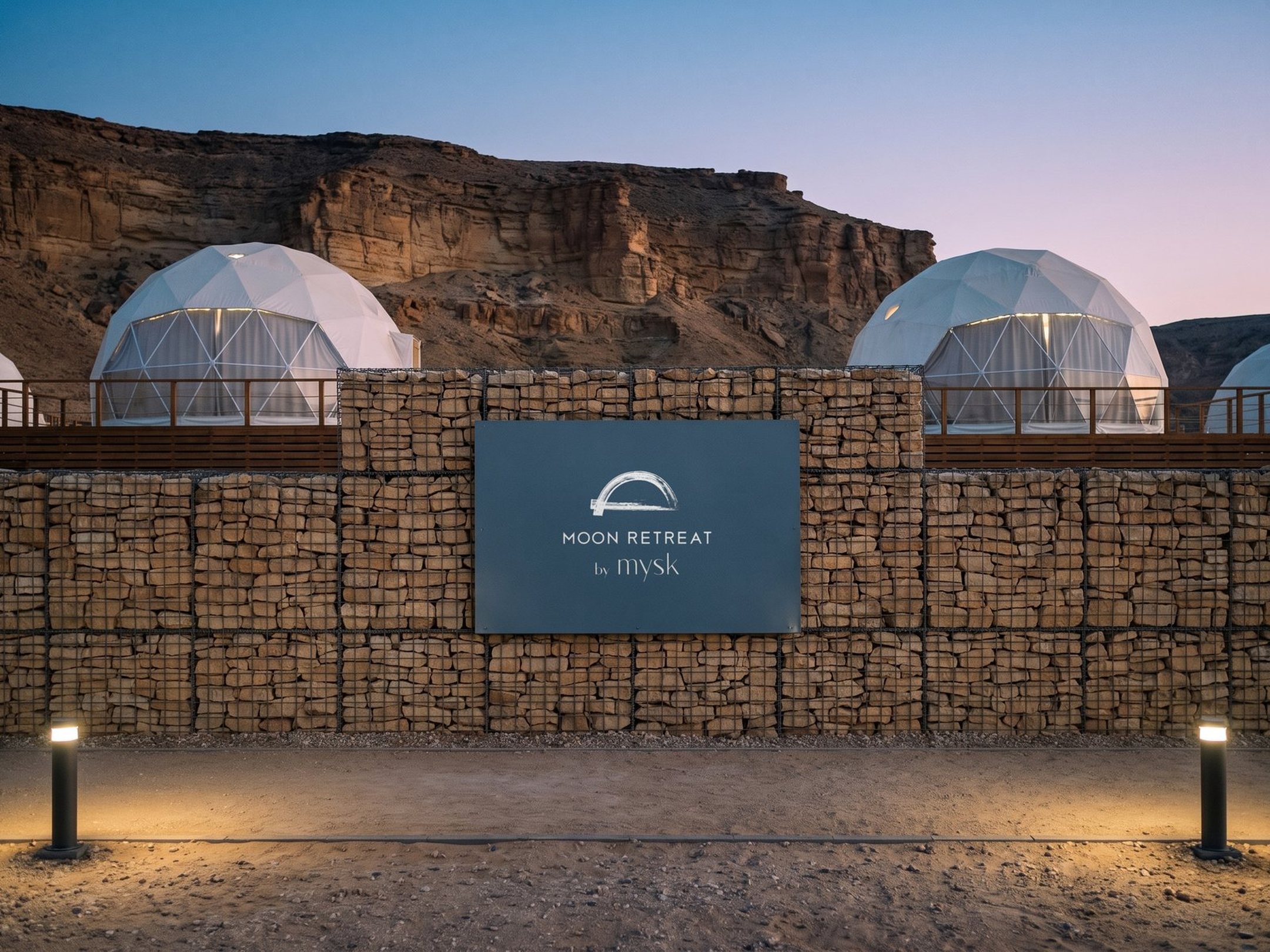 A render of the Moon Retreat lockup on a slate panel in a stone wall, domes behind, at blue hour