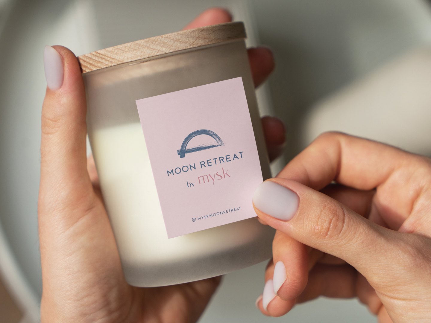 A frosted candle jar held in two hands, the Moon Retreat label on the front