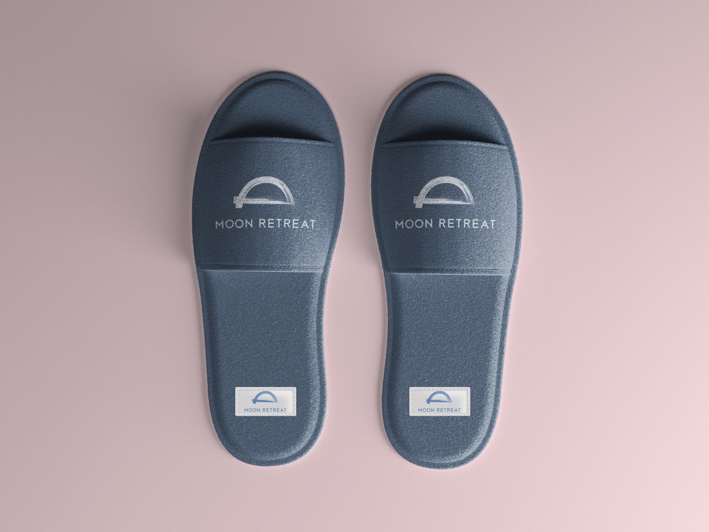 A pair of slate blue hotel slippers from above, the mark on each strap