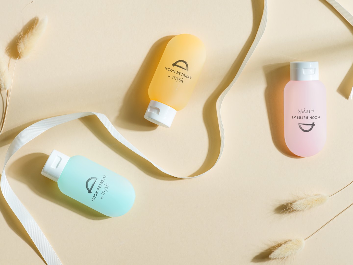 Three soft travel bottles in mint, apricot and pink on a pale yellow ground