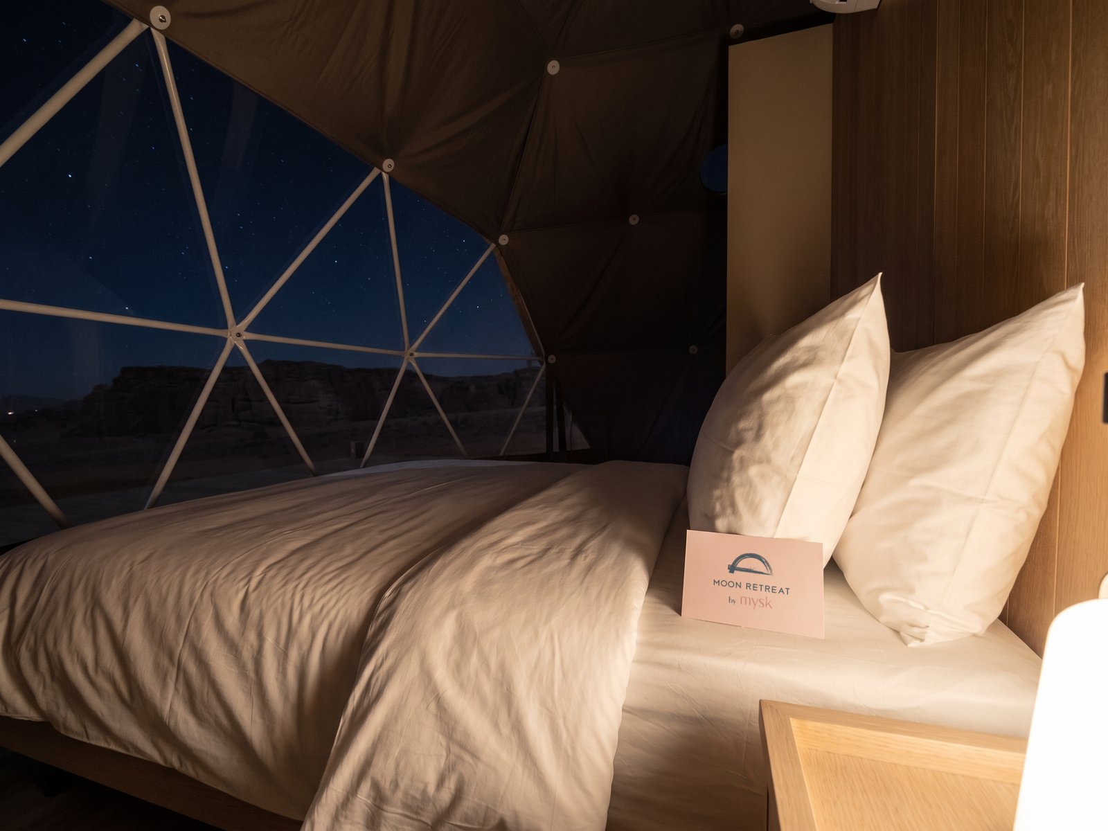 A render: a bed facing a clear dome panel at night, a pink card on the pillow