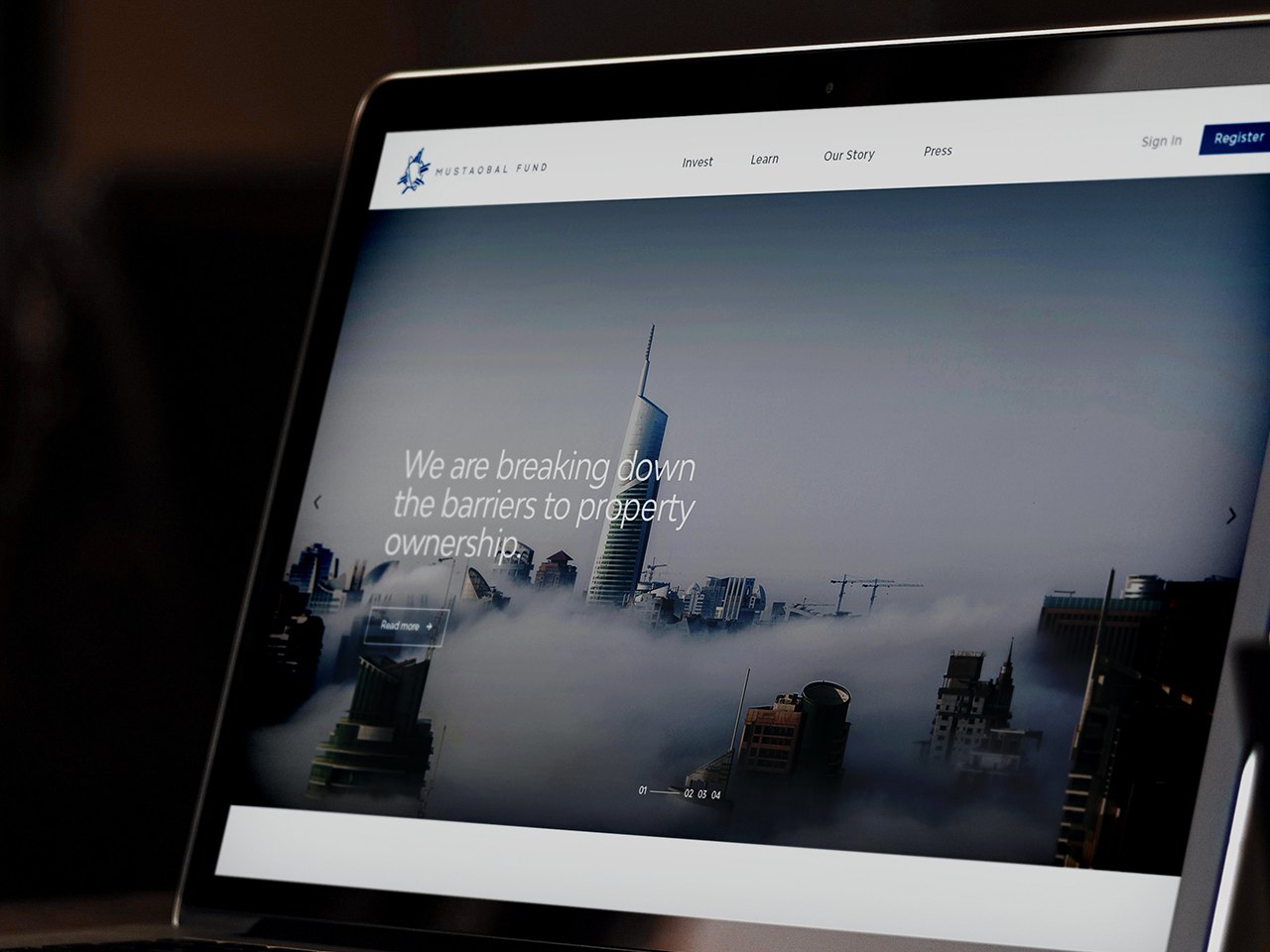 A laptop showing the Mustaqbal Fund home page: towers in fog and the line
