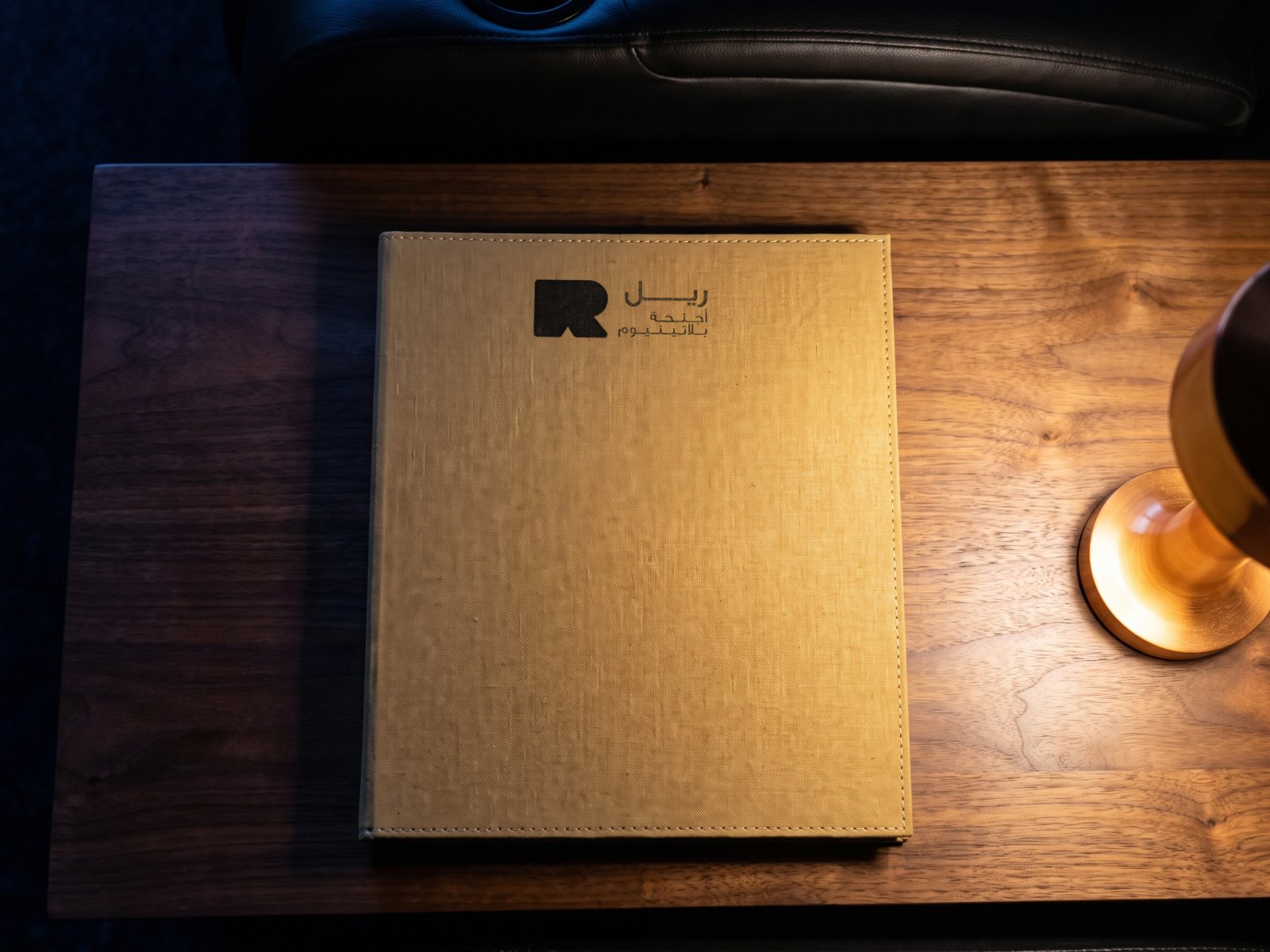 A render: the menu seen from above on a walnut table, the Arabic cover in the lamp's light