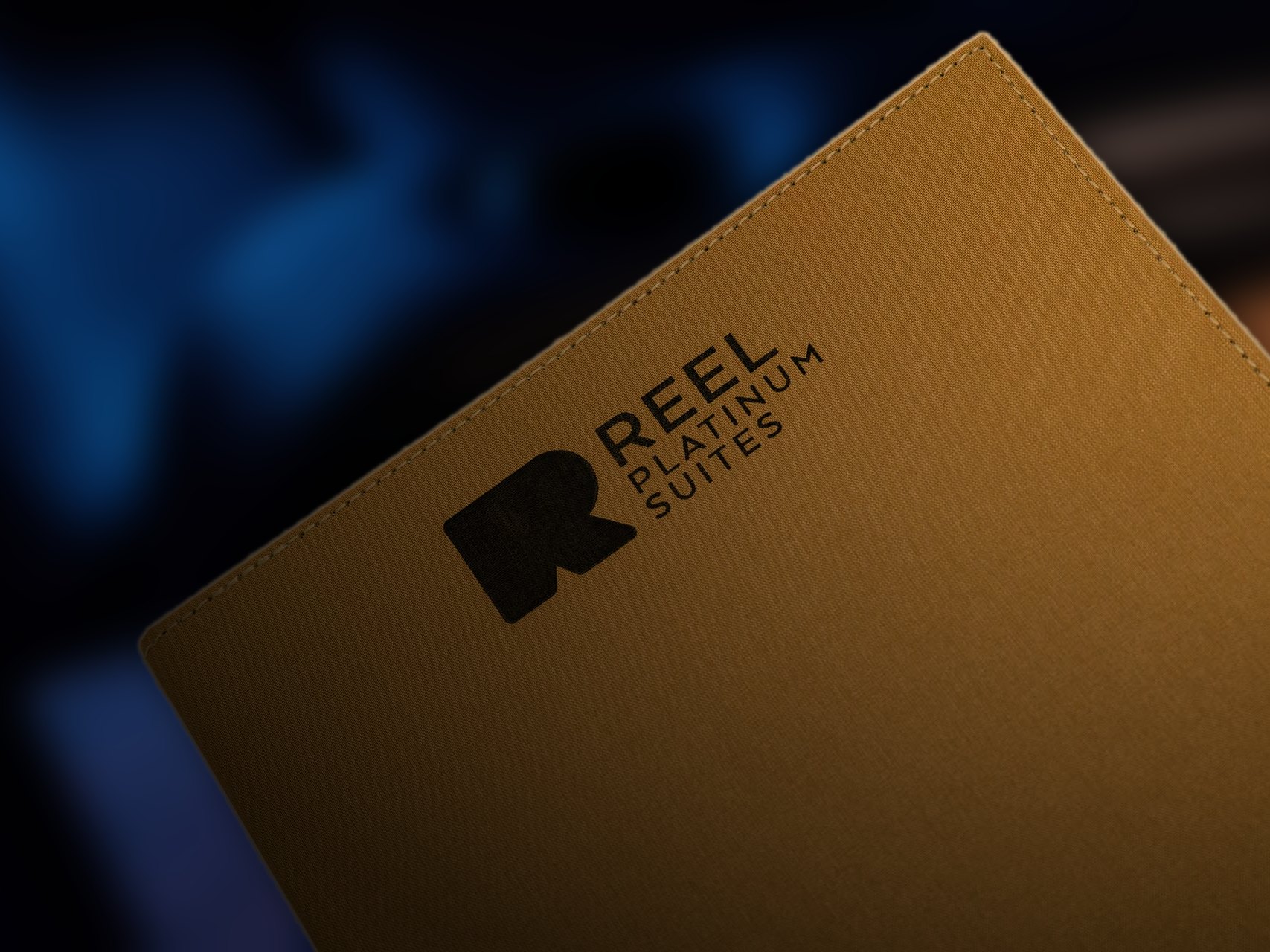 The gold linen menu cover with the Reel Platinum Suites mark, lit by a warm lamp in a dark room