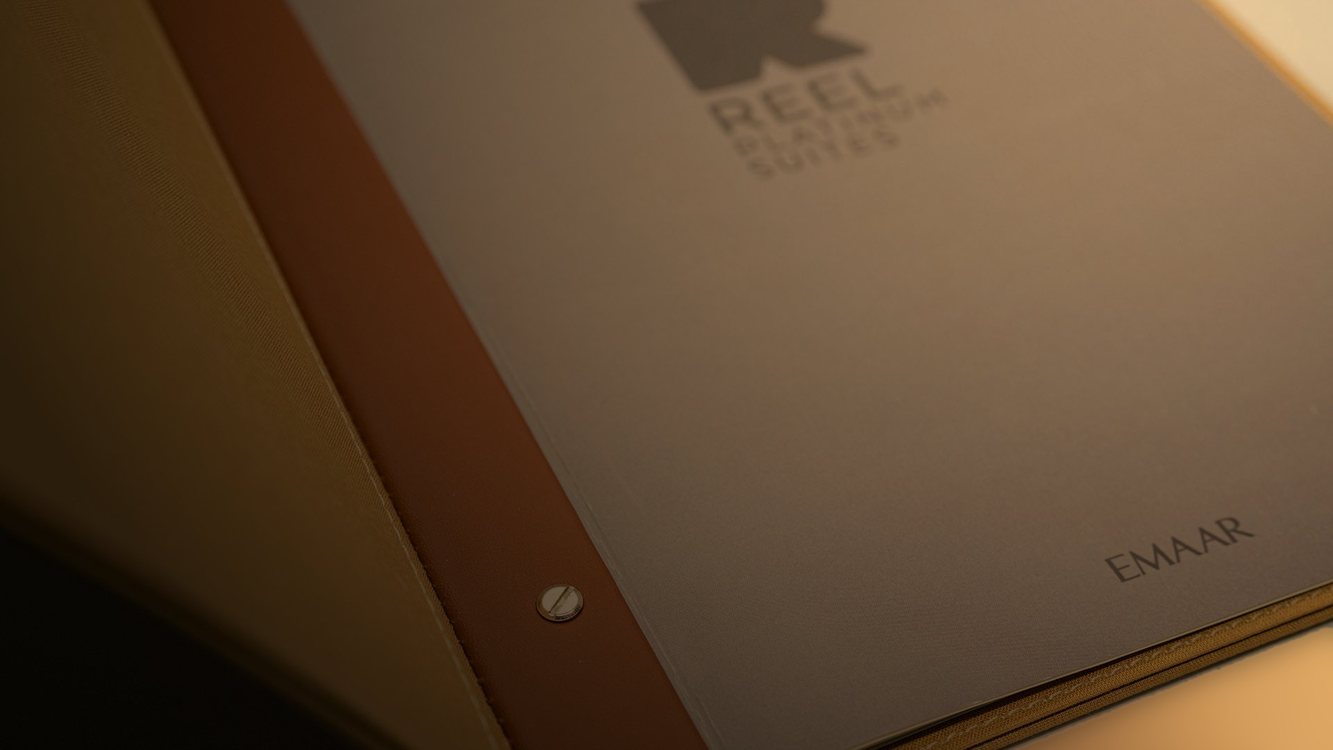 The menu's taupe inner cover with the mark and Emaar printed in tone, beside the leather strap, in low light