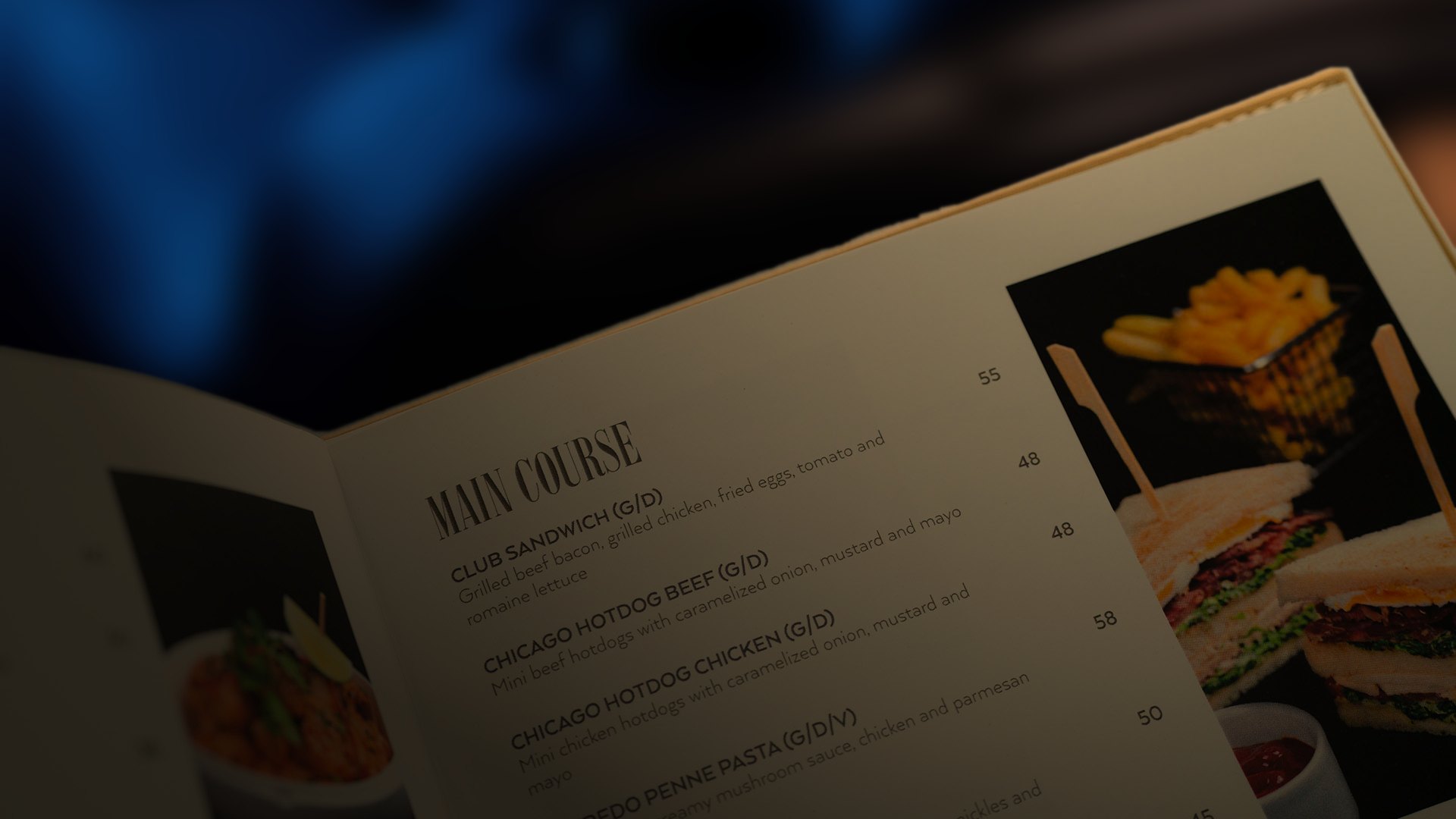 An open menu spread headed Main Course with photographs of a sandwich and fries, in warm low light