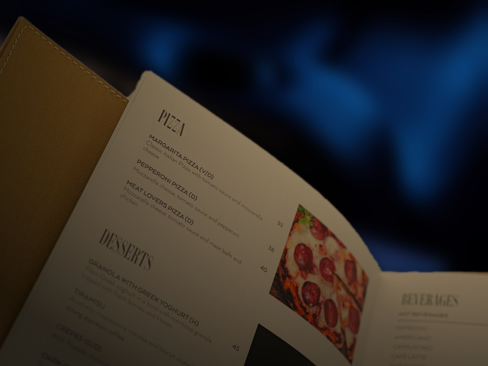 A menu page listing pizzas and desserts with a photograph of a pepperoni pizza, held up in a dark room