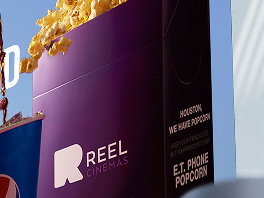 A purple popcorn bucket printed with the Reel Cinemas lockup and film lines about popcorn