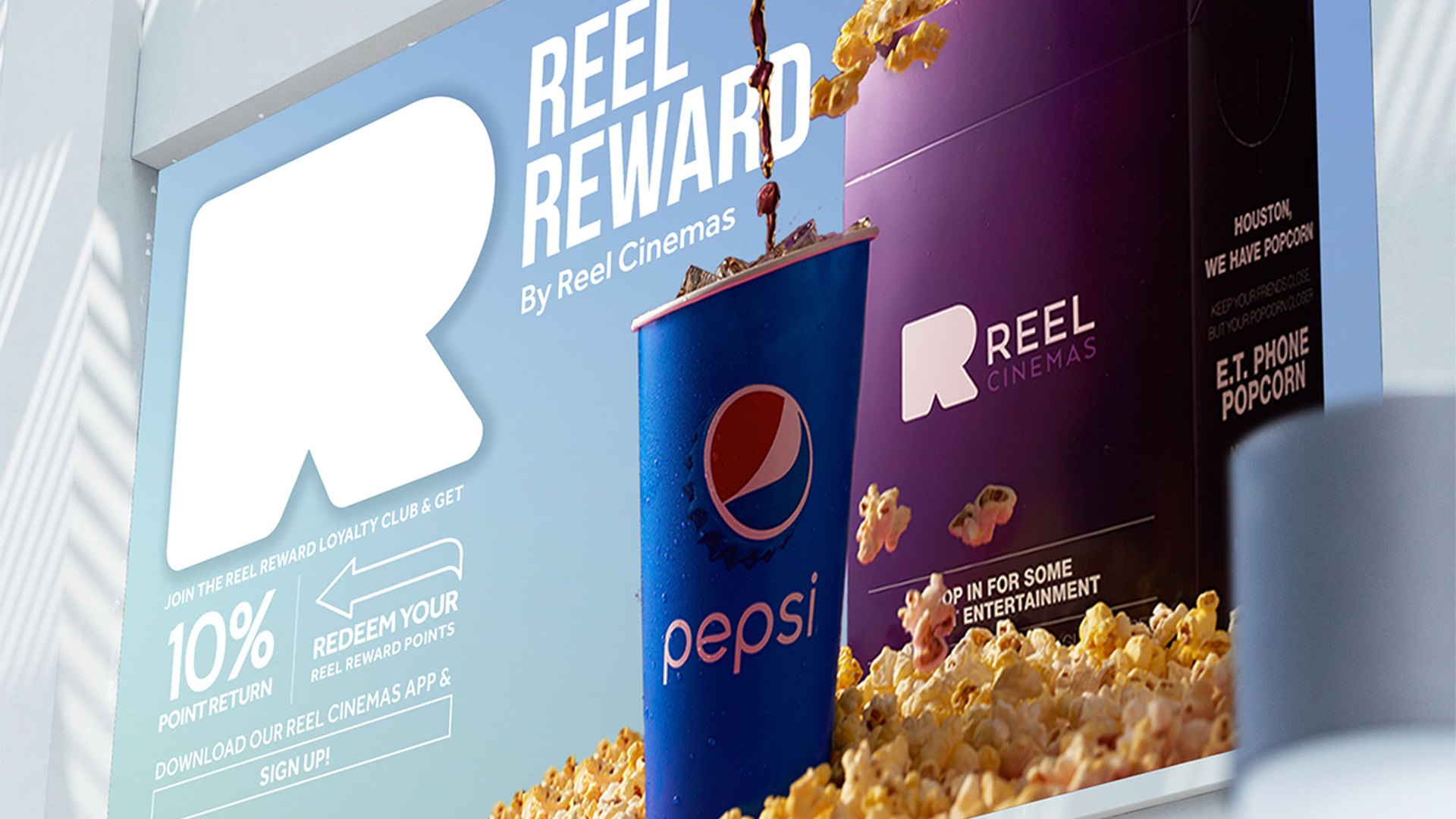 A billboard with the large white R, Reel Reward, a Pepsi cup and a purple popcorn bucket