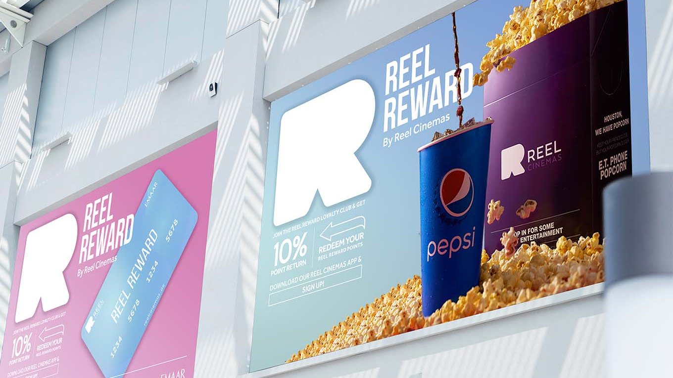 Two Reel Reward billboards, pink and sky blue, along the upper wall of a mall