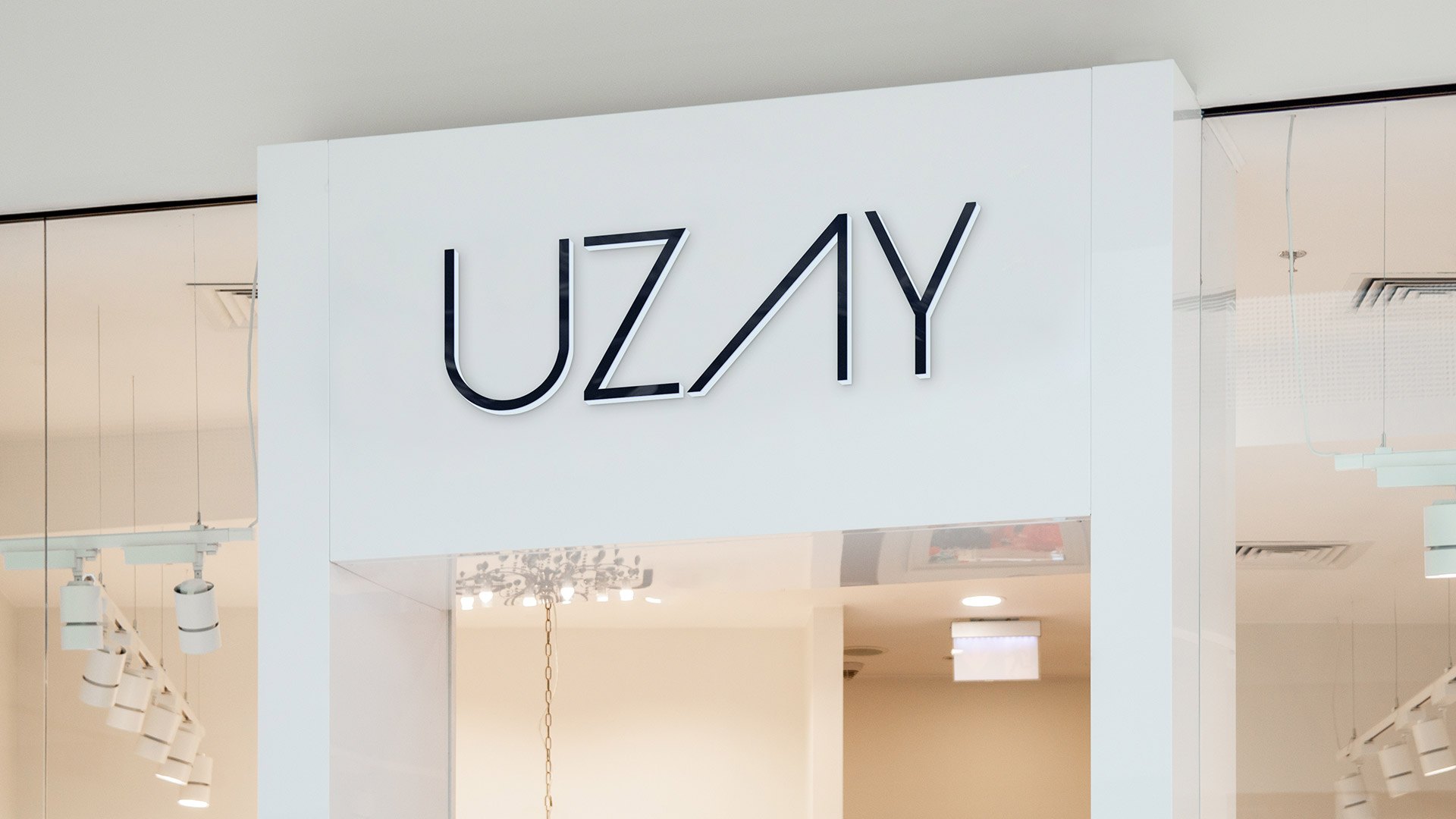 A white shopfront in a mall with the Uzay wordmark in dark letters on the fascia