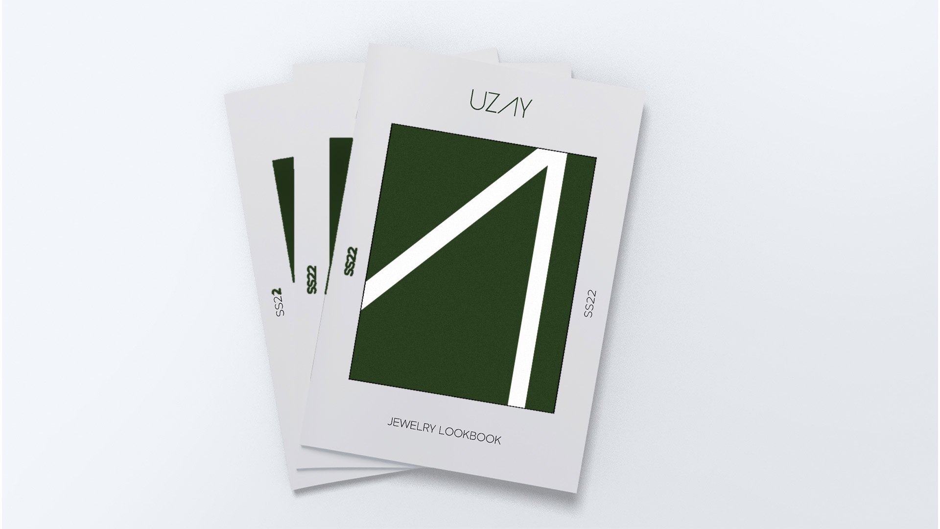Three Uzay lookbooks, the front cover showing a large white open A on olive
